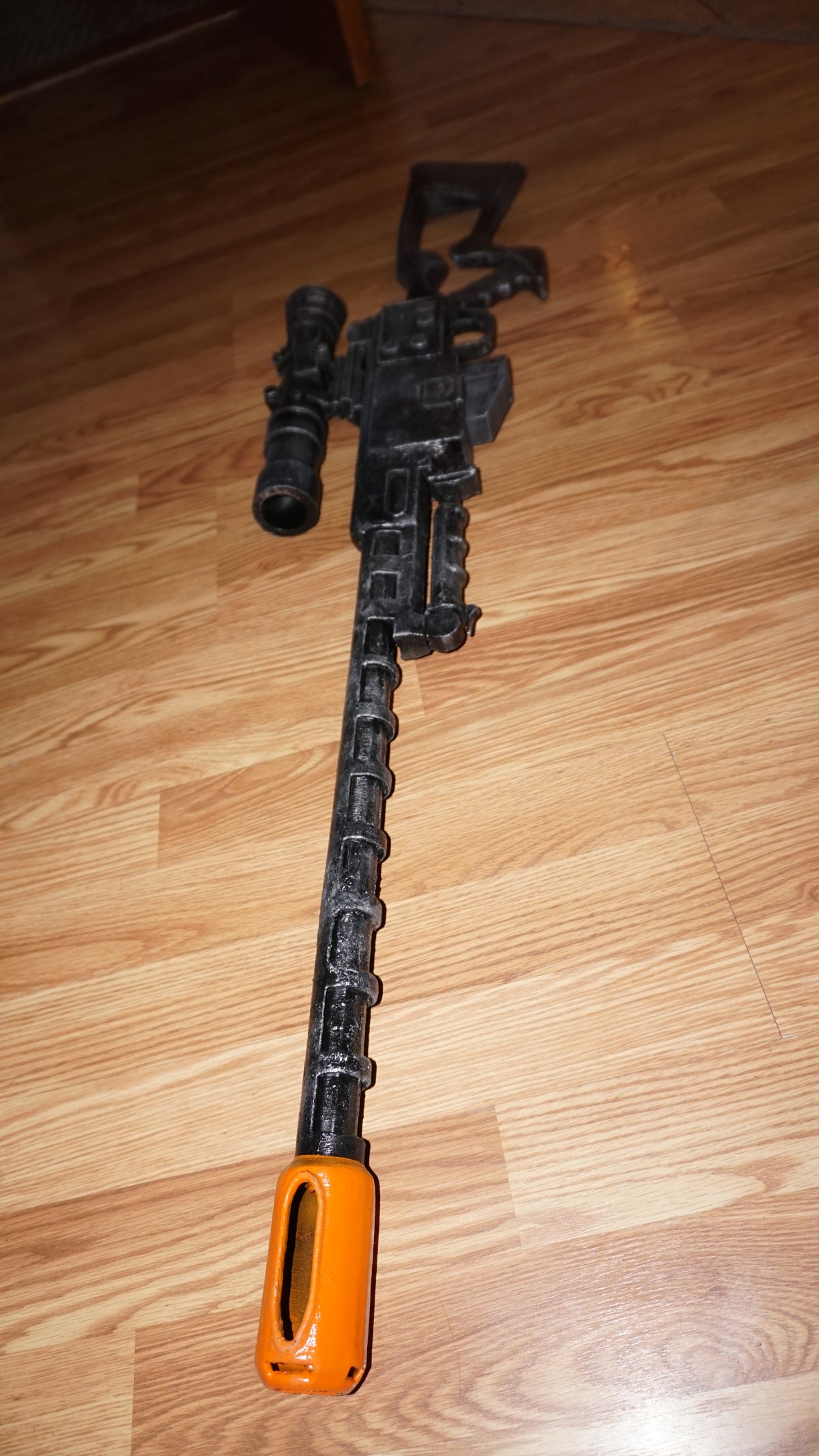 A black toy gun with an orange muzzle is lying on a wooden floor.