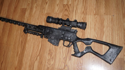 A black toy gun with a scope and a light attached to it, lying on a wooden floor.