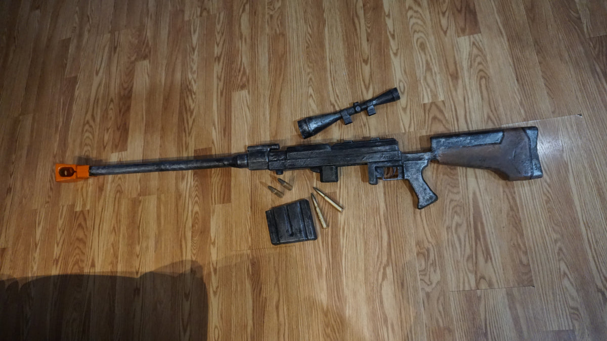 A black and silver toy rifle with a scope and a toy gun lying on a wooden floor.