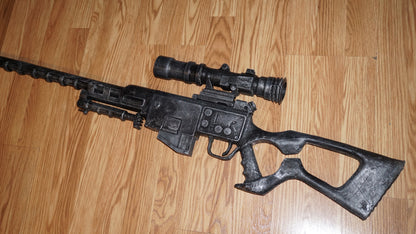A black toy gun with a scope and flash is lying on a wooden floor.